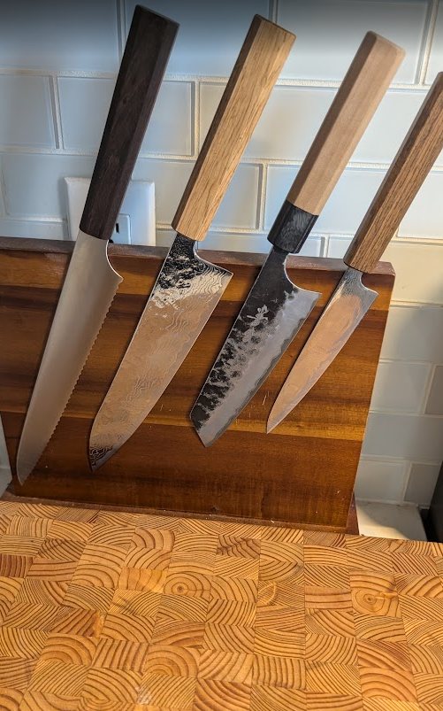Four kitchen knives displayed on an end-grain cutting board.